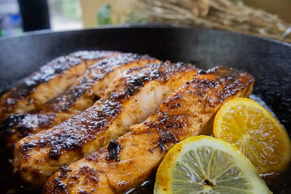 Grilled honey orange salmon with crispy skin in skillet, garnished with lemon slices. Perfect for seafood lovers.