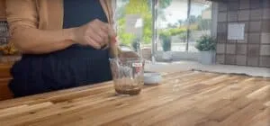 Person whisking sauce in a measuring cup in a bright kitchen setting.