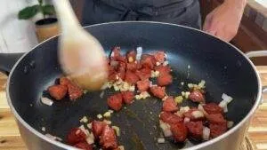 Cooking sausage and onions in a pan, stirred with a wooden spoon for a savory dish.