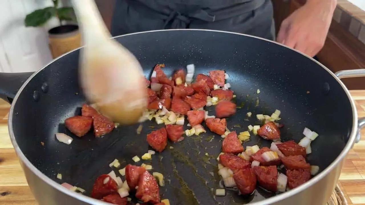 Cooking sausage and onions in a pan, stirred with a wooden spoon for a savory dish.