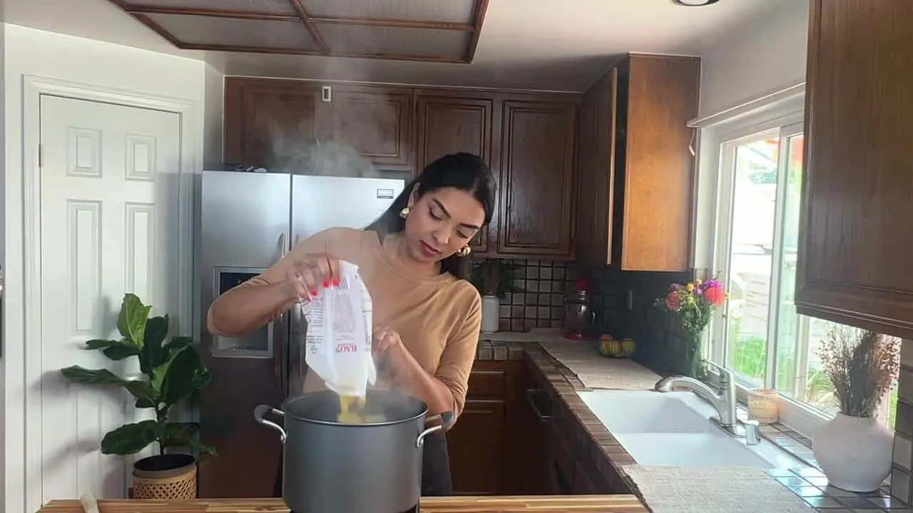Woman cooking pasta in a cozy kitchen with wooden cabinets and natural light.