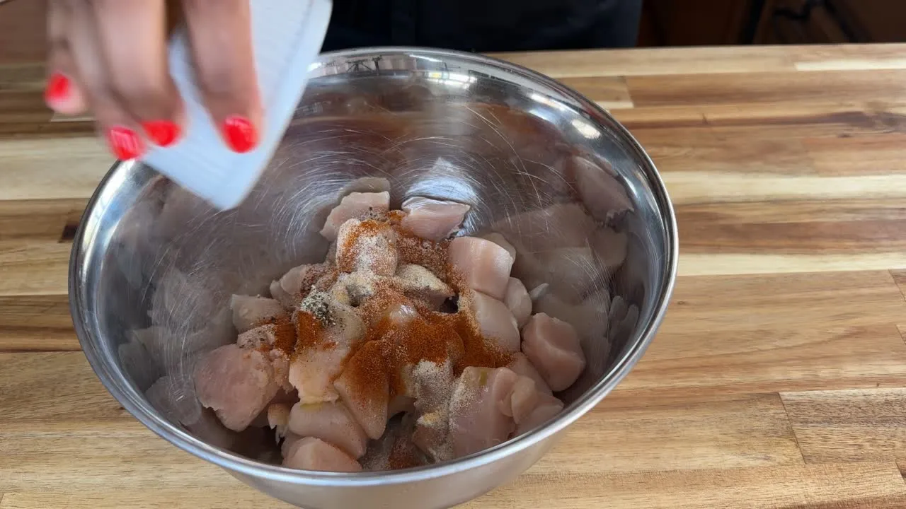 Seasoning raw chicken in a bowl with spices for a flavorful dish.