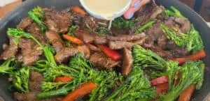 Stir-fried beef with broccoli and bell peppers in a skillet, with sauce being poured over for added flavor.