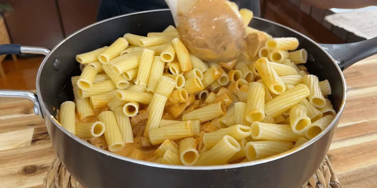 Creamy pasta dish being stirred in a pot on a wooden table. Perfect for hearty meal inspiration.