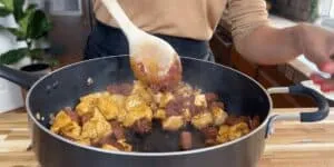 Cooking chicken and sausage in a skillet with wooden spoon, delicious homemade meal preparation in kitchen.
