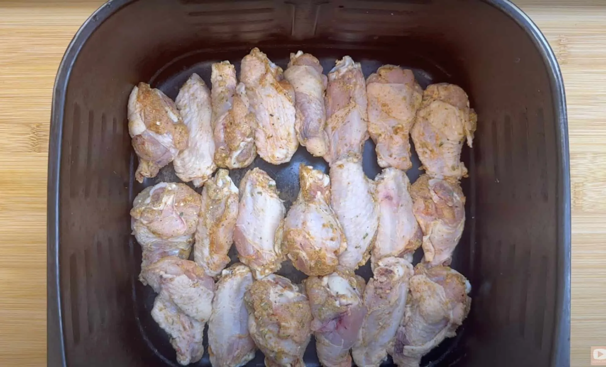 Raw marinated chicken wings in an air fryer tray, ready for cooking.