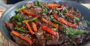 Sizzling beef stir-fry with red peppers and broccoli in a skillet, garnished with sesame seeds.