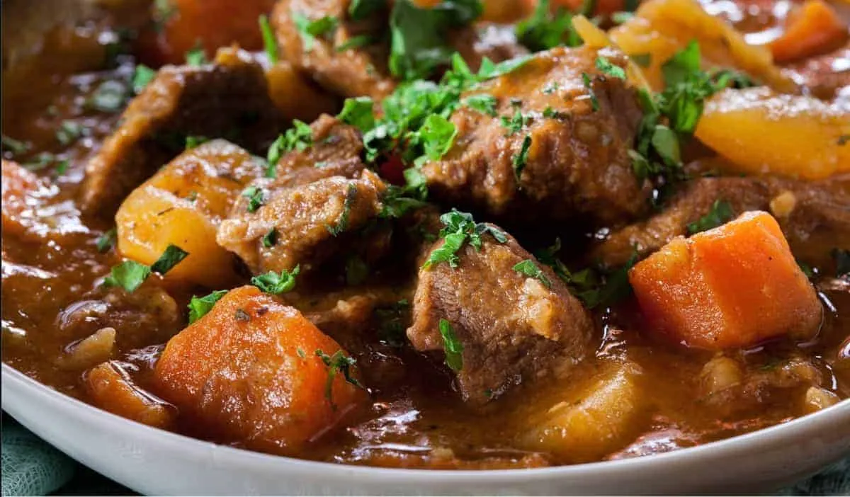 Hearty beef stew with carrots and potatoes, garnished with fresh parsley in a bowl, perfect for a cozy meal.