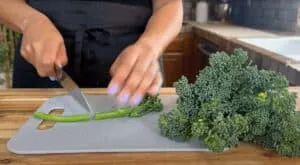 Person chopping fresh broccoli on a cutting board in a kitchen setting.