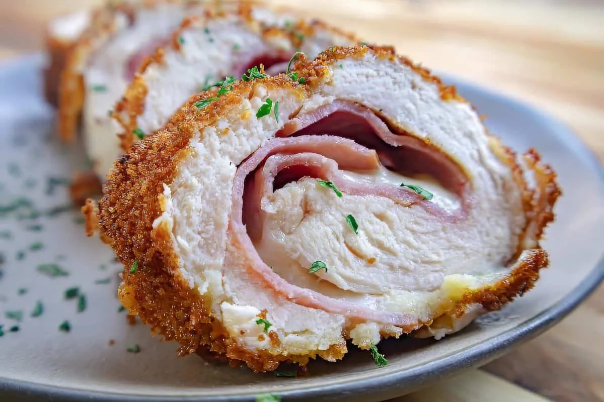 Close-up of sliced chicken cordon bleu with crispy breadcrumb coating, melted cheese, and ham on a plate.