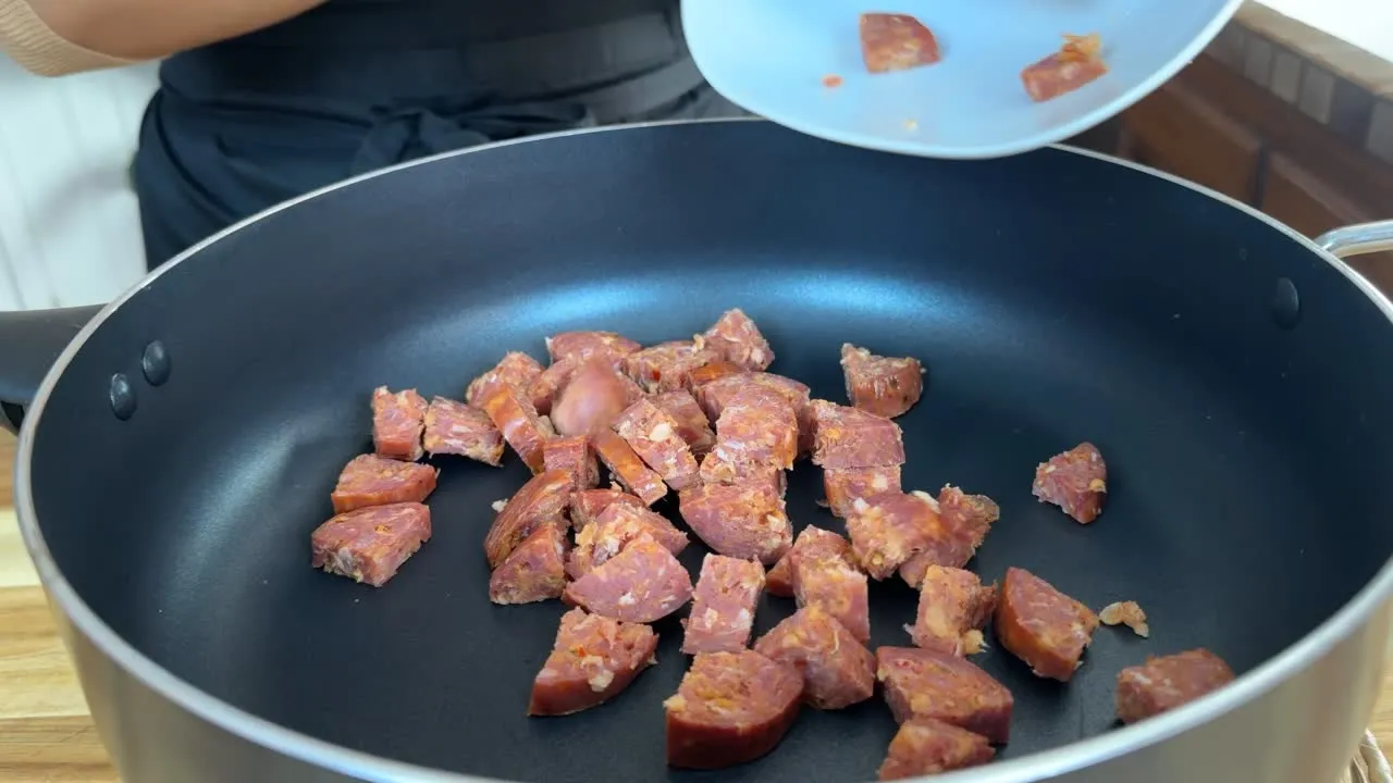 Diced sausage being added to a hot skillet for cooking, showing a step in a recipe preparation.