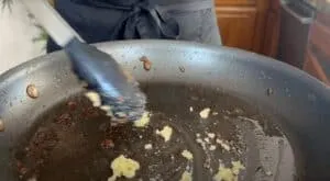 Tongs scrape food remnants from a nonstick pan surface in a kitchen setting.