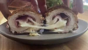 Close-up of crispy chicken cordon bleu sliced open with melted cheese and ham on a plate.