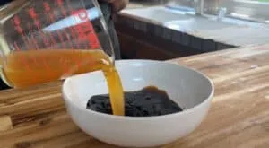 Pouring broth into a bowl of black beans on a wooden countertop in a kitchen setting.