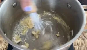 Stirring roux mixture in a pot on a stovetop, showing flour and butter combining.