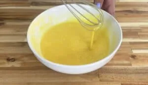 Whisking golden yellow batter in a white bowl on a wooden countertop, perfect for baking recipes.