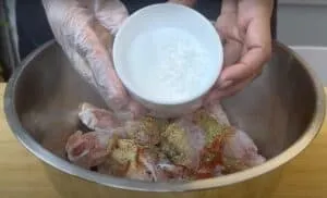 Mixing spices and cornstarch into raw chicken wings in a metal bowl for a flavorful dish preparation.