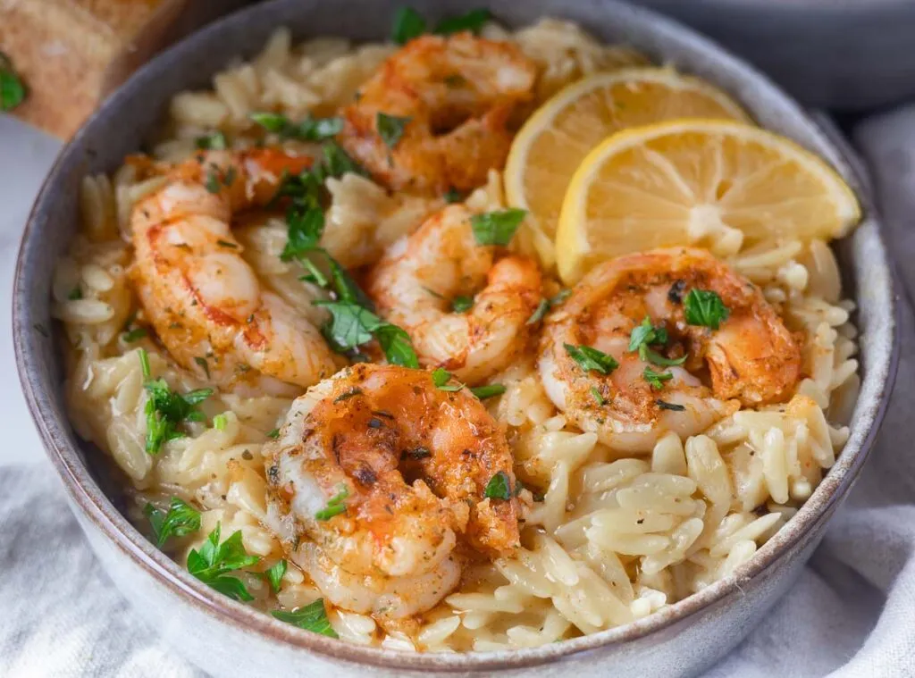 Shrimp scampi orzo in a bowl, garnished with parsley and lemon slices.