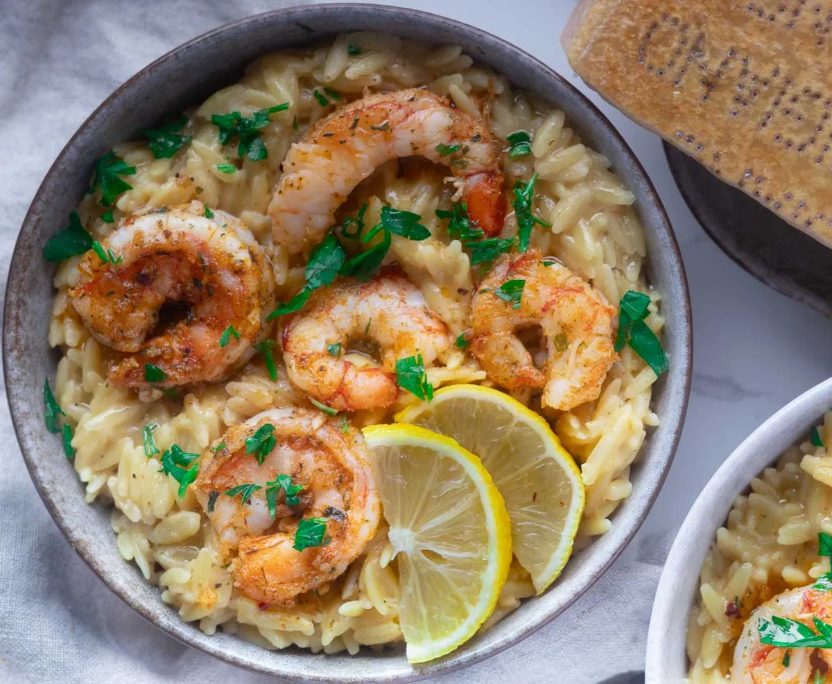 Shrimp scampi orzo with lemon slices and parsley on creamy orzo in a bowl.