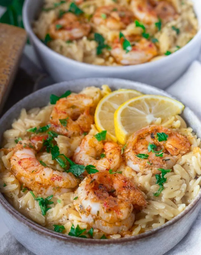 Shrimp scampi orzo with seasoned shrimp, garnished with parsley and lemon slices, served in a bowl.