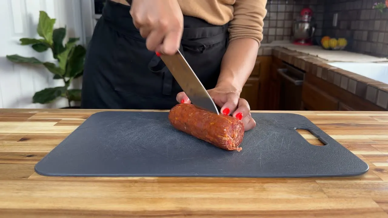 Person slicing a sausage on a cutting board in a kitchen.