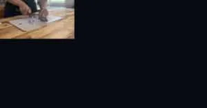 Person slicing onions with a knife on a wooden chopping board in a kitchen.