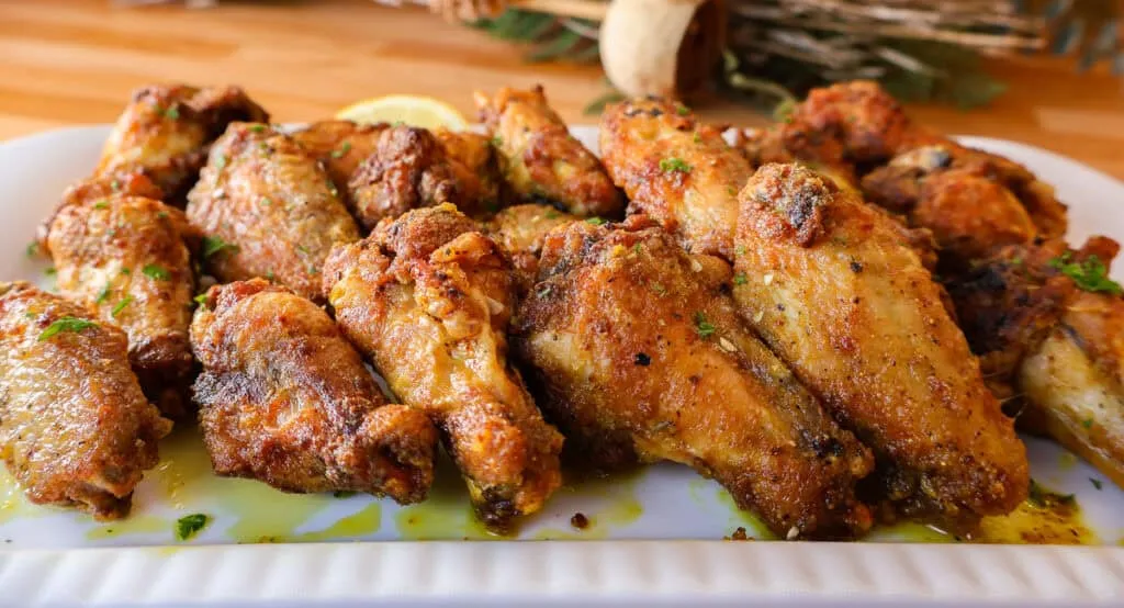 Crispy honey lemon pepper wings  with herbs and spices on a white platter.