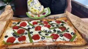 Freshly baked rectangular pizza with pepperoni, olives, and green peppers on parchment paper.