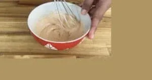 Whisking creamy peanut butter mixture in a red bowl on a wooden surface for a delicious recipe.