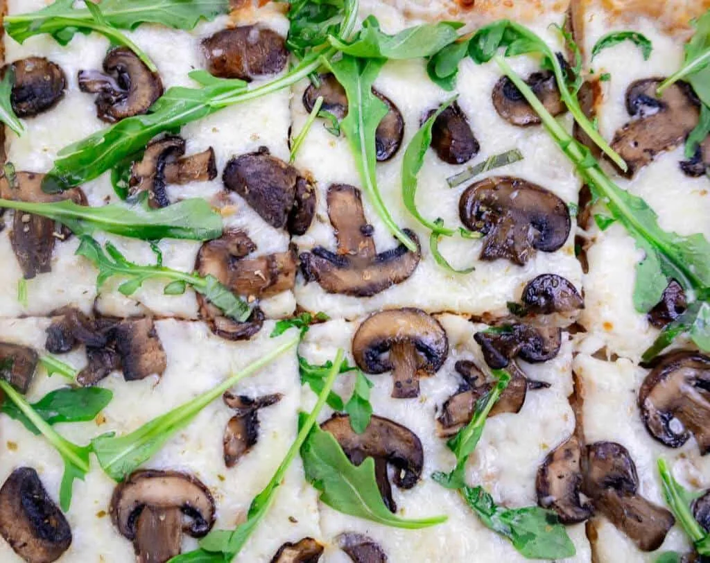 Close-up of a delicious Mushroom & White Sauce Puff Pastry pizza topped with melted cheese, fresh mushrooms, and arugula leaves.