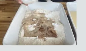 Mixing spices and flour in a white dish for baking preparation.