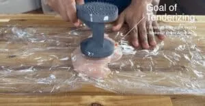 Tenderizing chicken with a mallet on a wooden board, enhancing softness and even cooking.
