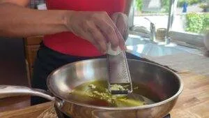Grating fresh garlic into olive oil in a pan, enhancing flavor for a delicious dish. Cooking preparation in action.