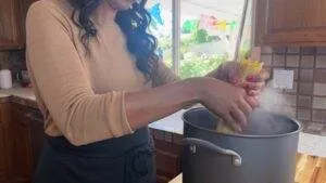 Woman cooking pasta in a pot on a stove in a bright kitchen.