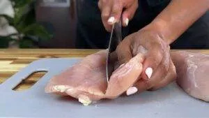 Slicing raw chicken breast on a cutting board for meal preparation.