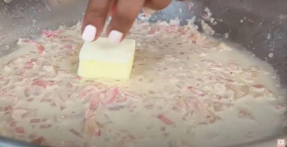 Adding butter to creamy onion sauce in a pan, enhancing flavor and texture.