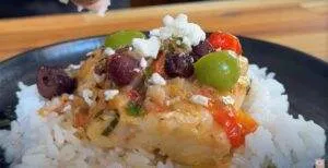 Delicious baked fish with olives, tomatoes, and feta on rice, served on a plate. Perfect Mediterranean dish.
