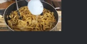 Cooking tagliatelle pasta with ground meat and sauce in a pan, water being added for a creamy texture.