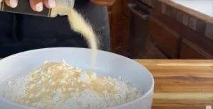 Pouring seasoning onto flour in a white bowl for cooking preparation on a wooden countertop.