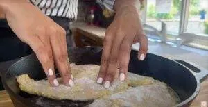 Cooking chicken in a cast iron skillet, hands pressing down seasoned chicken breasts in a kitchen.
