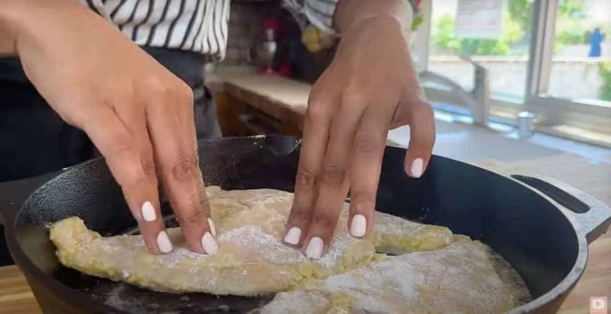 Cooking chicken in a cast iron skillet, hands pressing down seasoned chicken breasts in a kitchen.
