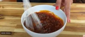 Whisking homemade spicy sauce in a white bowl on a wooden countertop.