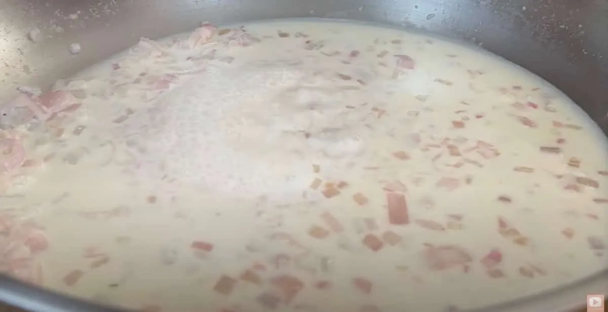 Creamy sauce with diced onions and ham simmering in a pan.