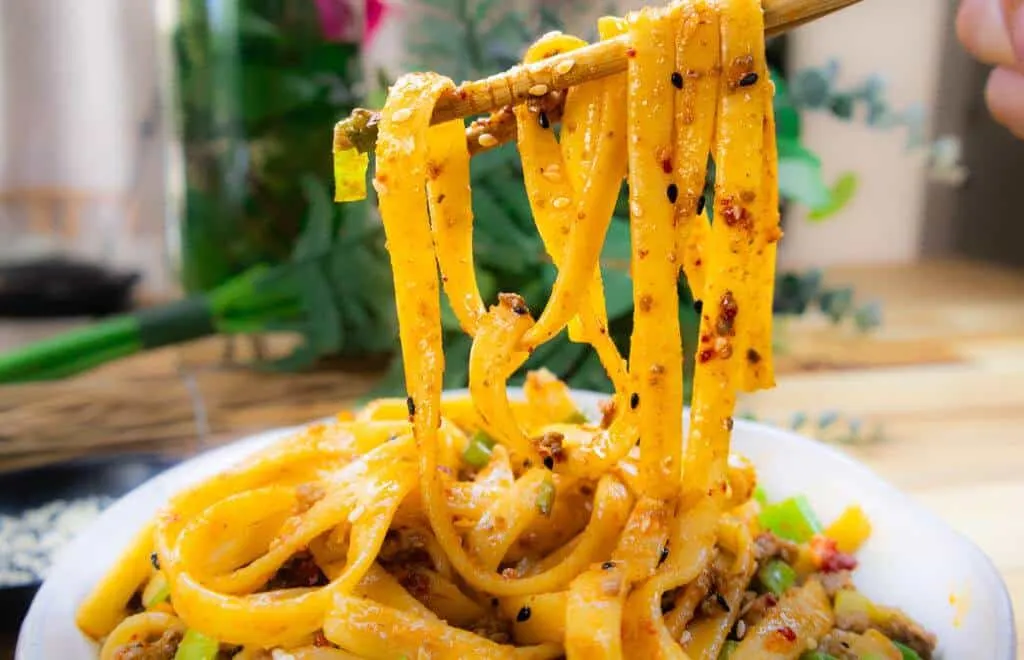Spicy noodles with sesame seeds and vegetables lifted by chopsticks in a delicious Asian dish.