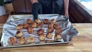 Person holding a baking tray of freshly cooked meatballs on foil in the kitchen.