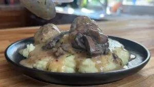 Creamy mashed potatoes topped with savory mushroom gravy on a black plate.