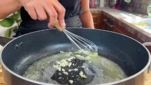 Person cooking garlic in a pan with a whisk.