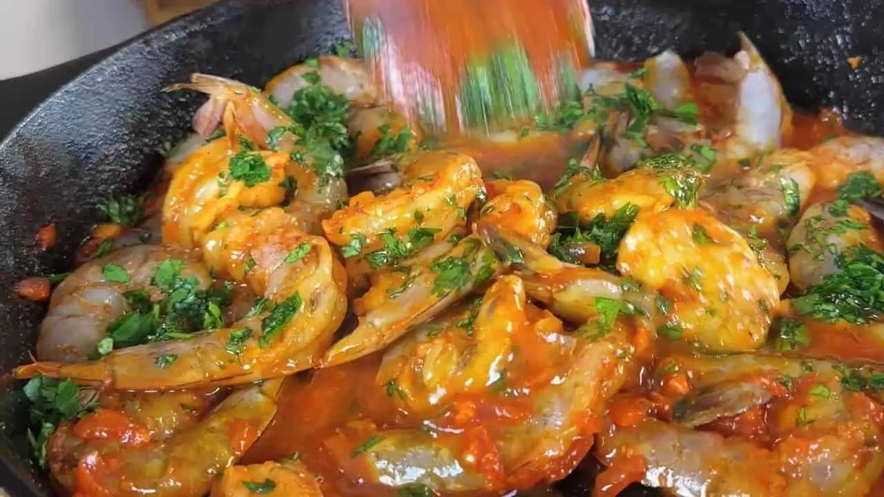 Spicy peri peri shrimp cooking in a skillet with fresh herbs and vibrant sauce. Ideal for seafood lovers.
