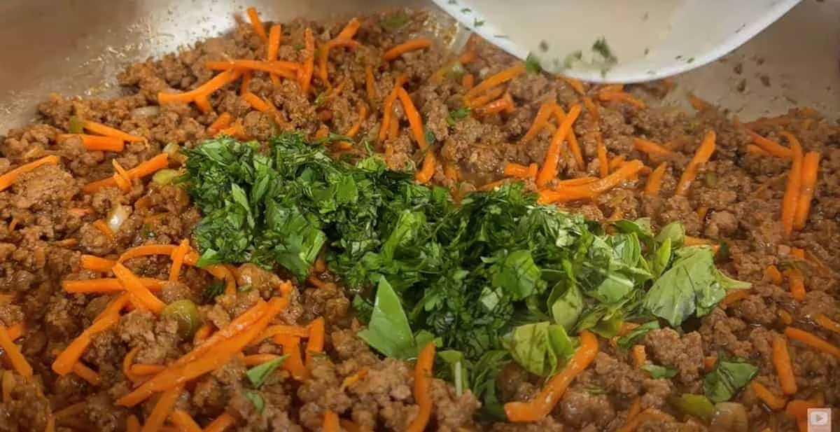 Ground beef with carrots and fresh herbs in a pan, perfect for tasty homemade tacos or a flavorful dinner base.