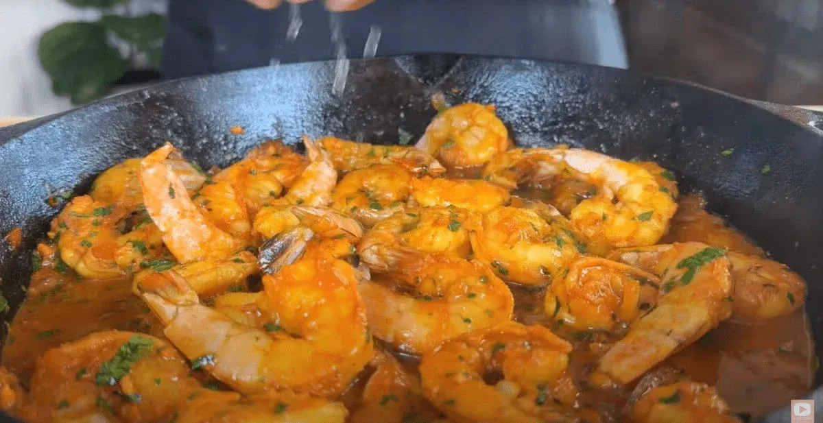 Sizzling peri peri shrimp in garlic tomato sauce with herbs in a cast iron skillet, a flavorful seafood delicacy being garnished.